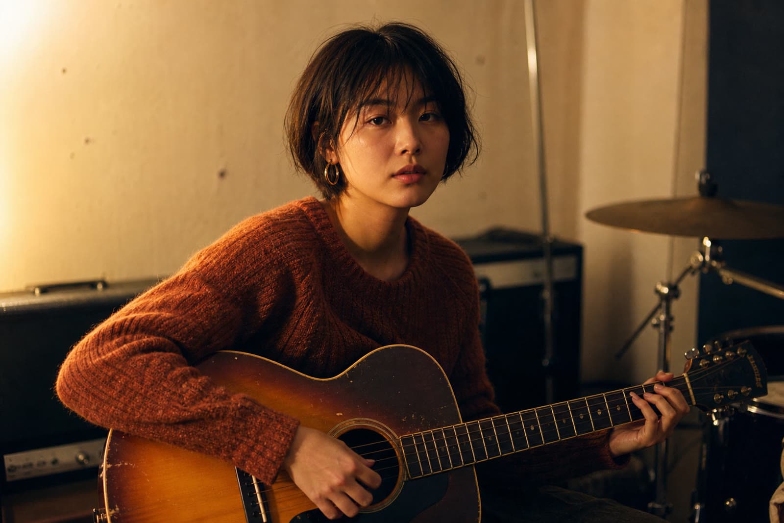 Noa Ellison holding a guitar in a rehearsal room